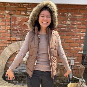 Puffer vest with plaid lining and fake fur-lined hood. Hood can unzip from vest